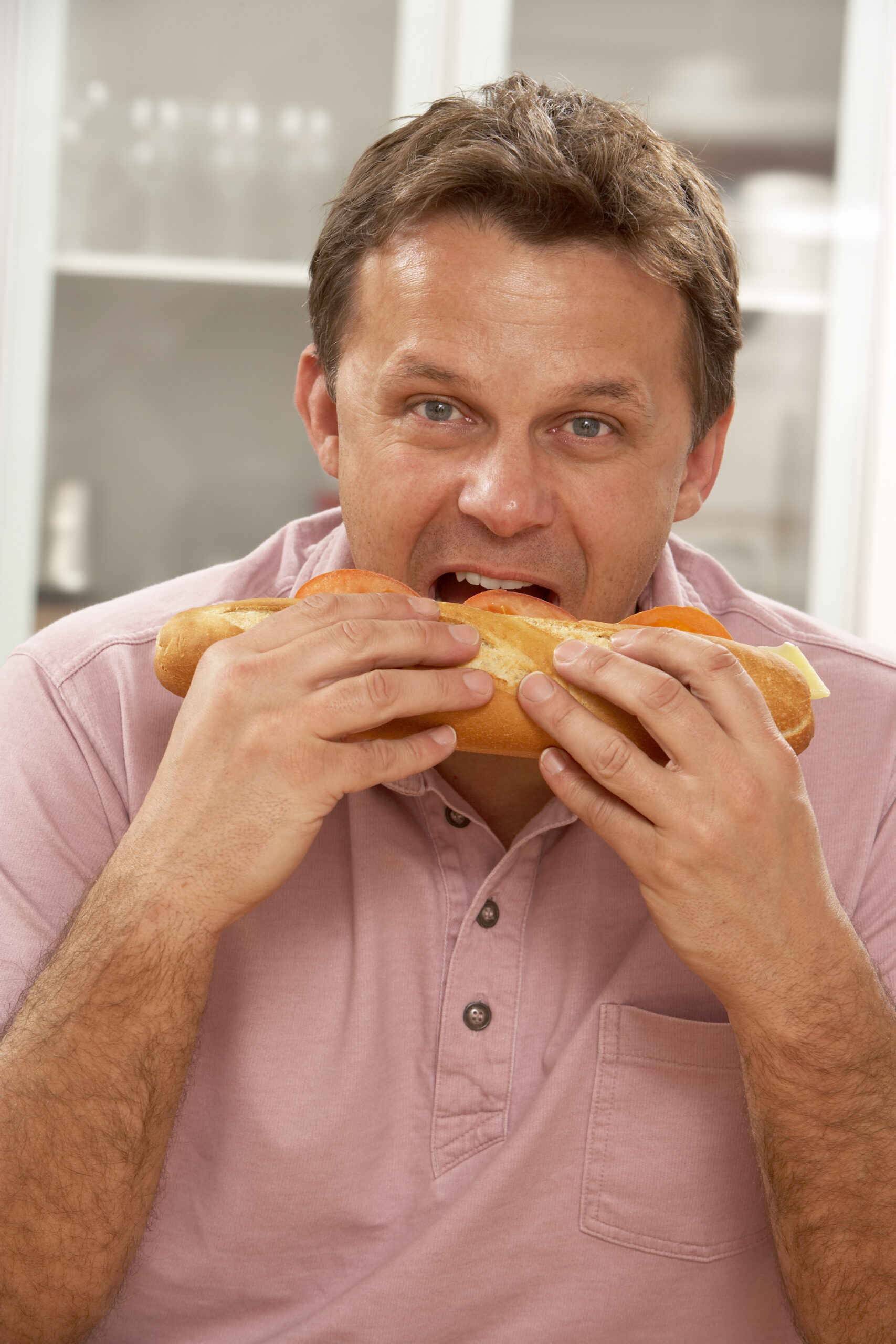 A man eating a submarine sandwich like an ear of corn
